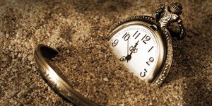 A pocket watch is buried in the dirty sand.